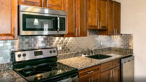 A kitchen with wooden cabinets, a stainless steel microwave, a stove, and a granite countertop. - Shadow Palm Villa 3 Private Resort Villa (Port Aransas)