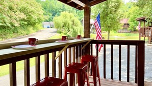 A wooden deck with a view of a road and greenery, a flag, and a table with a cup and saucer.