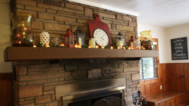 A fireplace with a stone mantle, adorned with decorative items like candles, lanterns, and a clock. - Midpines Hwy 140 House on your way to Yosemite (Midpines)