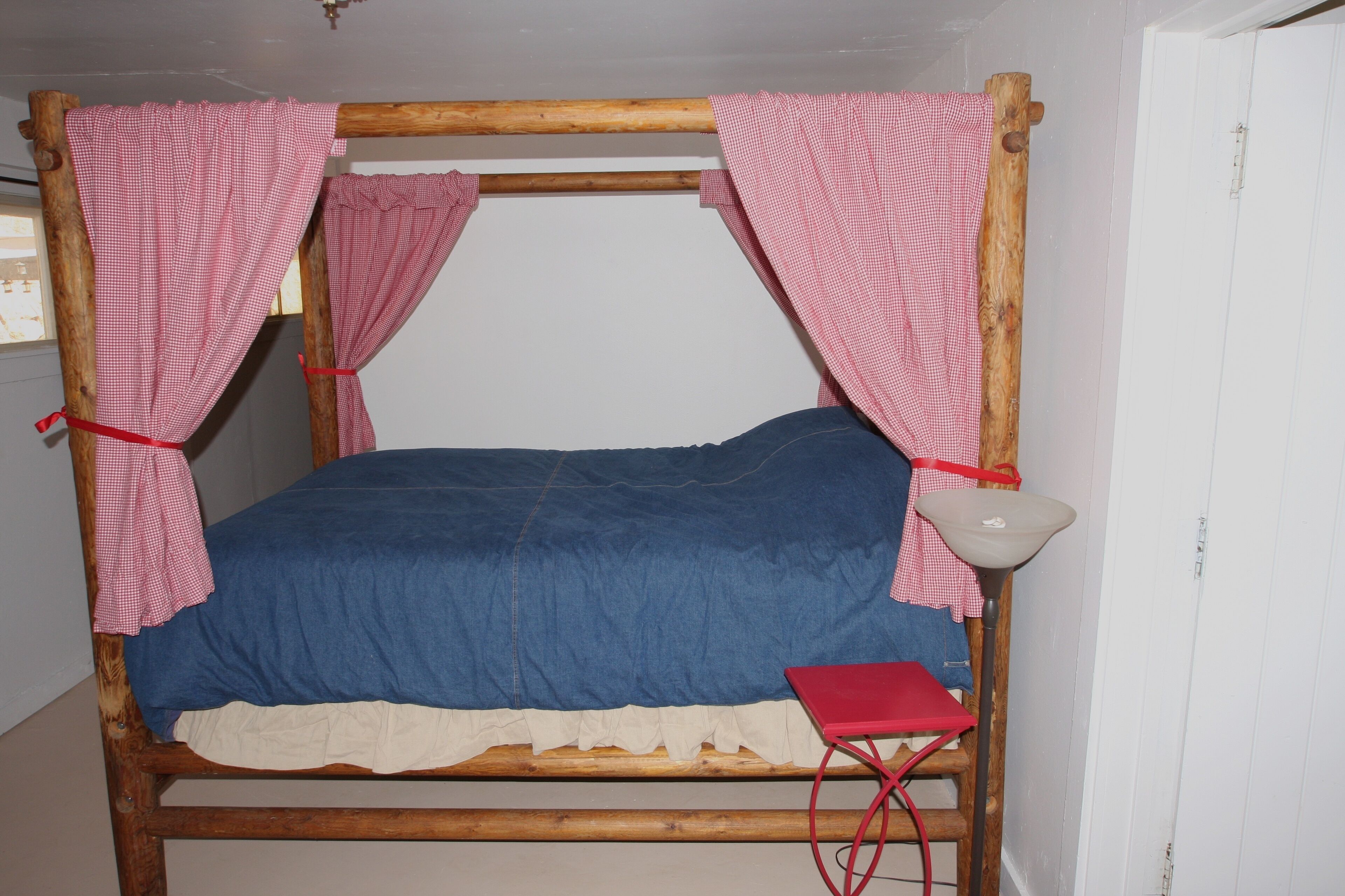 A wooden bed with a blue mattress and a red and white checkered canopy.