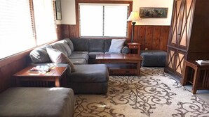 A living room with a sectional sofa, ottoman, wooden coffee table, patterned rug, and a small side table. - Midpines Hwy 140 House on your way to Yosemite (Midpines)