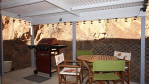 An outdoor patio with a wooden table and chairs, a barbecue grill, and string lights. - Midpines Hwy 140 House on your way to Yosemite (Midpines)