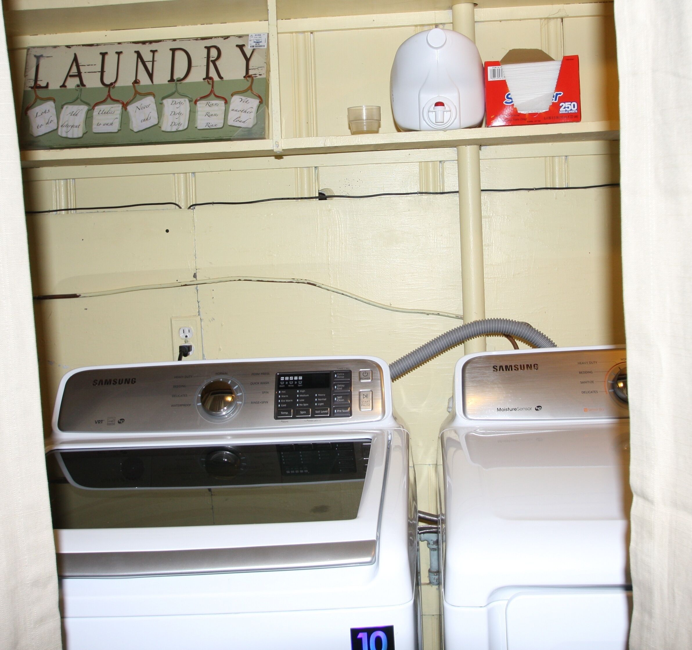 A laundry area with two washing machines, a shelf with a 'Laundry' sign, and a box of tissues.