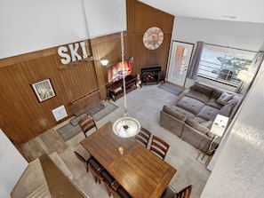 A cozy living room with a fireplace, a wooden wall with 'SKI' letters, a dining area, and a large window. - Ski-In/Out Giant Steps Condo | Sleeps 12 (Brian Head)
