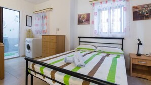 A bedroom with a bed, a washing machine, a wooden wardrobe, a nightstand, and a window with curtains. - Modern, Bright and spacious Apartment close to beach and st. Julians (Naxxar)