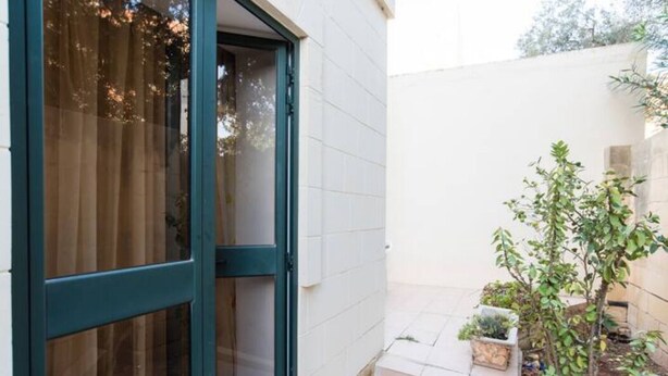 A building with a large glass door and a small garden area with plants. - Modern, Bright and spacious Apartment close to beach and st. Julians (Naxxar)