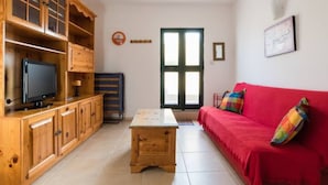 A living room with a wooden cabinet, a television, a red sofa, and a window with blinds. - Modern, Bright and spacious Apartment close to beach and st. Julians (Naxxar)