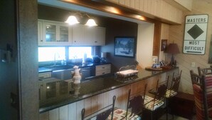 A kitchen with white cabinets, a black countertop, and a bar area with chairs. There is a sign on the wall that reads "MASTERS MOST DIFFICULT".