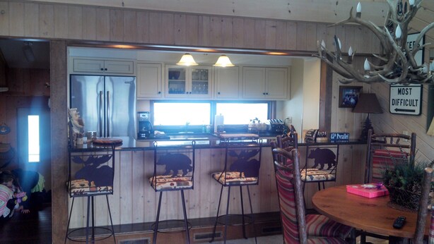 A kitchen with wooden cabinets, a refrigerator, a coffee maker, and a bar area with stools.