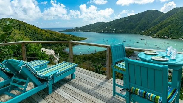 Eine Terrasse mit türkis-farbenen Möbeln mit Blick auf eine Bucht und Boote.