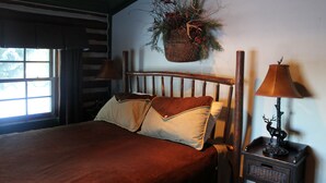 A bed with a brown bedspread and two pillows, a nightstand with a lamp, and a hanging basket with greenery on the wall. - Charming Log Cabin In Beautiful Cottonwood Canyon, Just Outside of Bozeman (Bozeman)