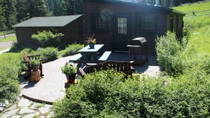A wooden cabin with a patio, surrounded by greenery and mountains. - Charming Log Cabin In Beautiful Cottonwood Canyon, Just Outside of Bozeman (Bozeman)
