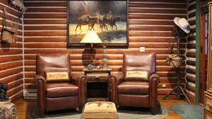 A log cabin interior with two leather armchairs, a small table with a lamp, a painting of horses, and a mounted cowboy hat. - Charming Log Cabin In Beautiful Cottonwood Canyon, Just Outside of Bozeman (Bozeman)