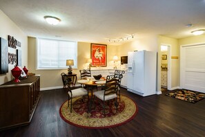 Un espacio habitable compacto con zona de comedor que incluye una mesa redonda y cuatro sillas, un refrigerador, un microondas y una ventana con persianas.