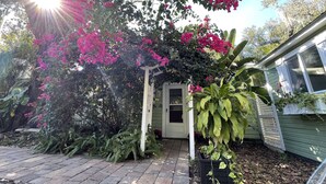 A garden with a pergola covered in pink flowers, a pathway, and a house with a window.