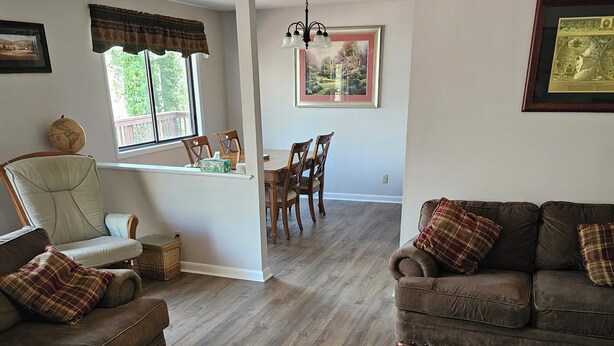 Un salon avec un canapé marron, un fauteuil assorti et une table à manger en bois avec des chaises. Une grande fenêtre laisse entrer la lumière naturelle, et on peut apercevoir un globe sur le mur.