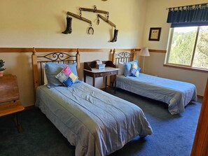 A room with two beds, a small table, and a window with a view of trees.