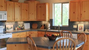 A kitchen with wooden cabinets, a microwave, a stove, a dining table with chairs, and a fruit basket.