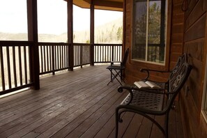 A wooden cabin with a porch, two metal chairs, and a window.