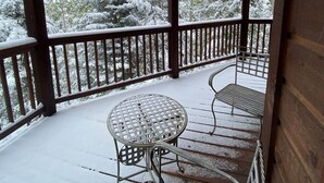 A wooden deck with a metal table and bench, surrounded by snow-covered trees.