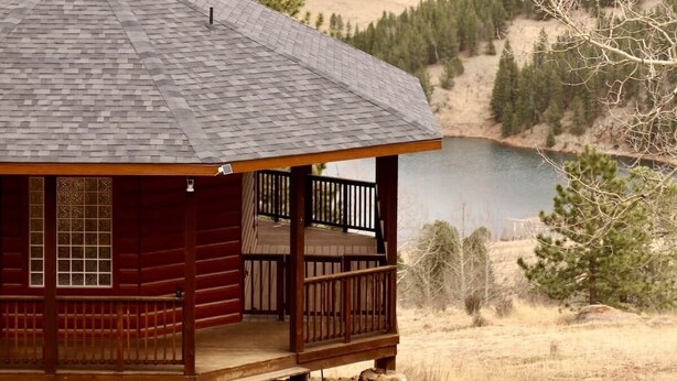 A cabin with a porch, a view of a lake, and forested hills in the background.