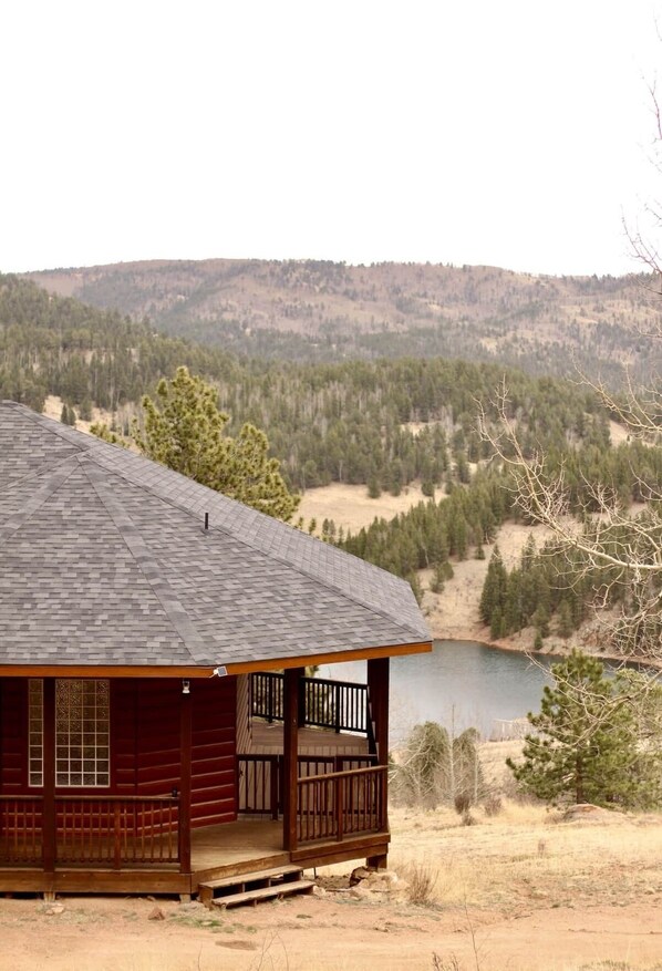A cabin with a porch, a view of a lake, and forested hills in the background.