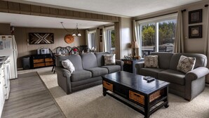 Ein Wohnzimmer mit zwei grauen Sofas, einem Couchtisch und einem Küchenbereich im Hintergrund.