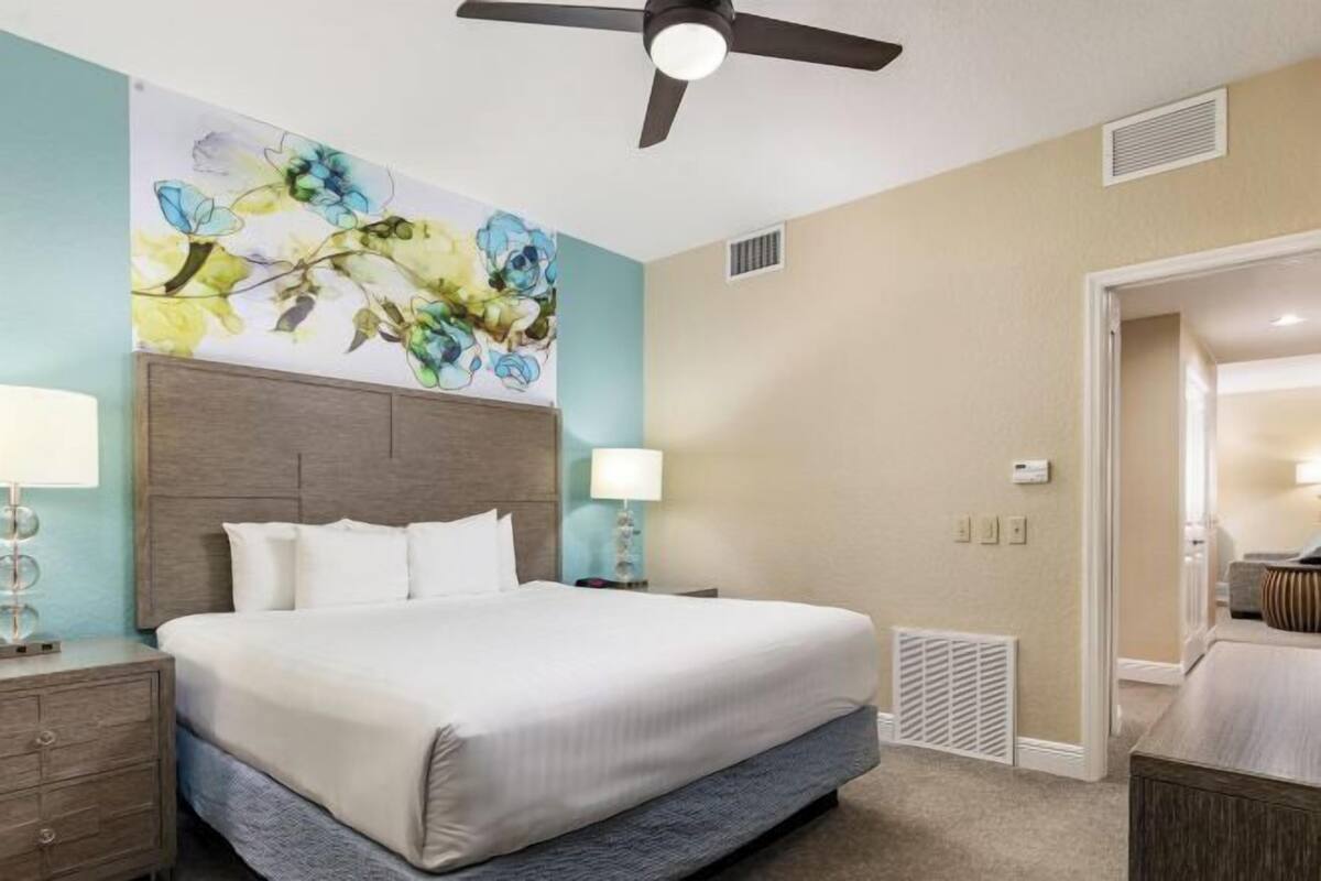 A hotel room with a bed, two bedside tables, a ceiling fan, a radiator, and a door leading to another room.