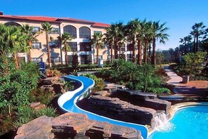 Un complexe hôtelier doté d’un espace piscine agrémenté d’une fontaine sinueuse, de palmiers et d’un bâtiment à plusieurs étages avec des balcons.