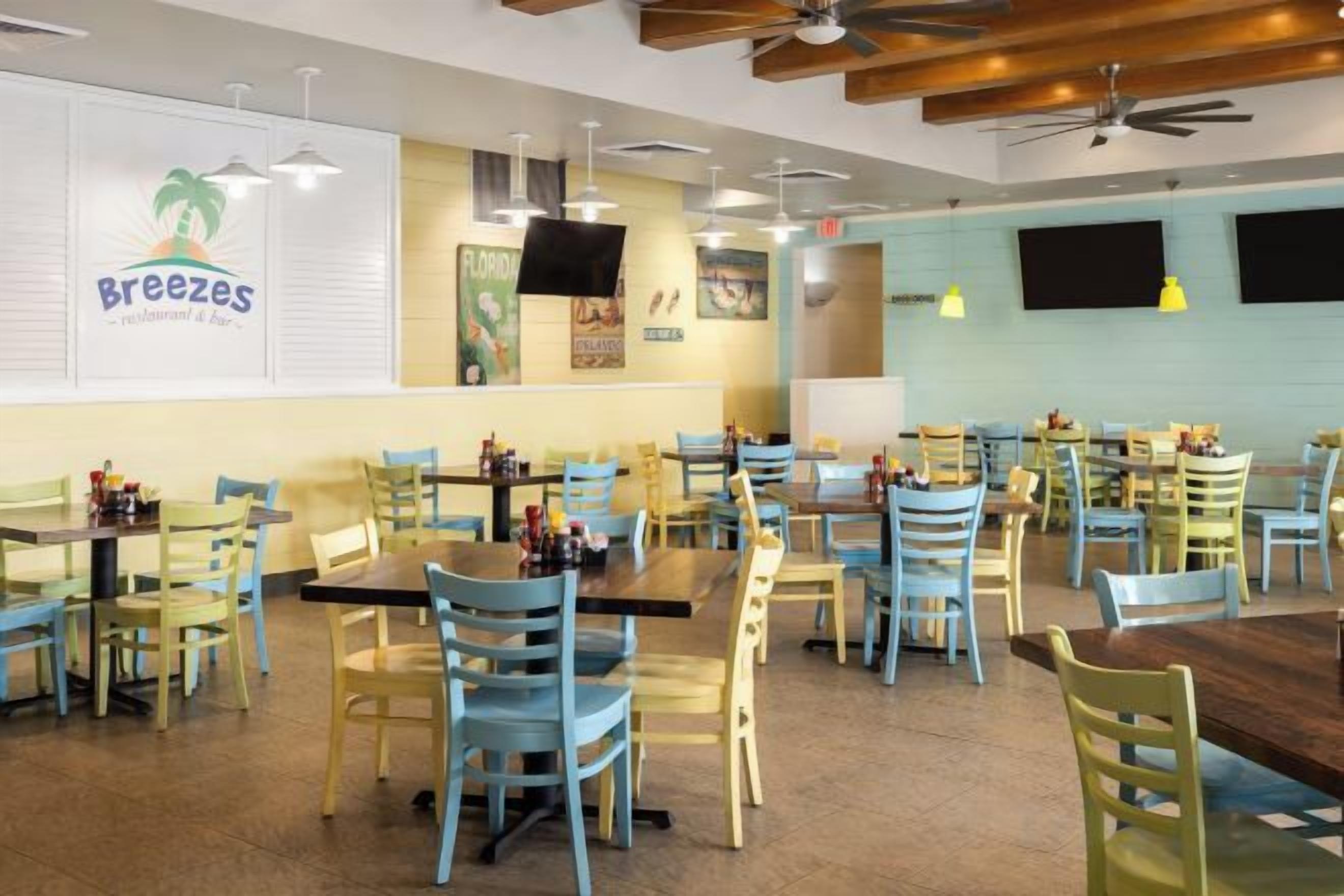Um restaurante com várias mesas e cadeiras, um ventilador de teto e um quadro de cardápio na parede.