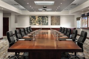 Sala de conferências com uma mesa comprida, várias cadeiras e um projetor.