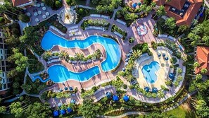Vue aérienne d’un complexe hôtelier doté de plusieurs piscines, de chaises longues et de palmiers.