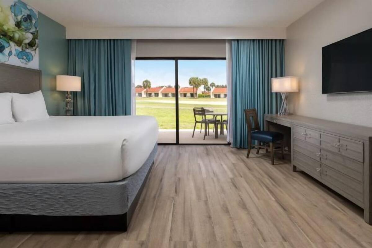 A hotel room with a bed, a desk, a chair, a TV, and a view of a courtyard.