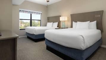 Quarto de hotel com duas camas, uma escrivaninha, ventilador de teto e janela com vista.