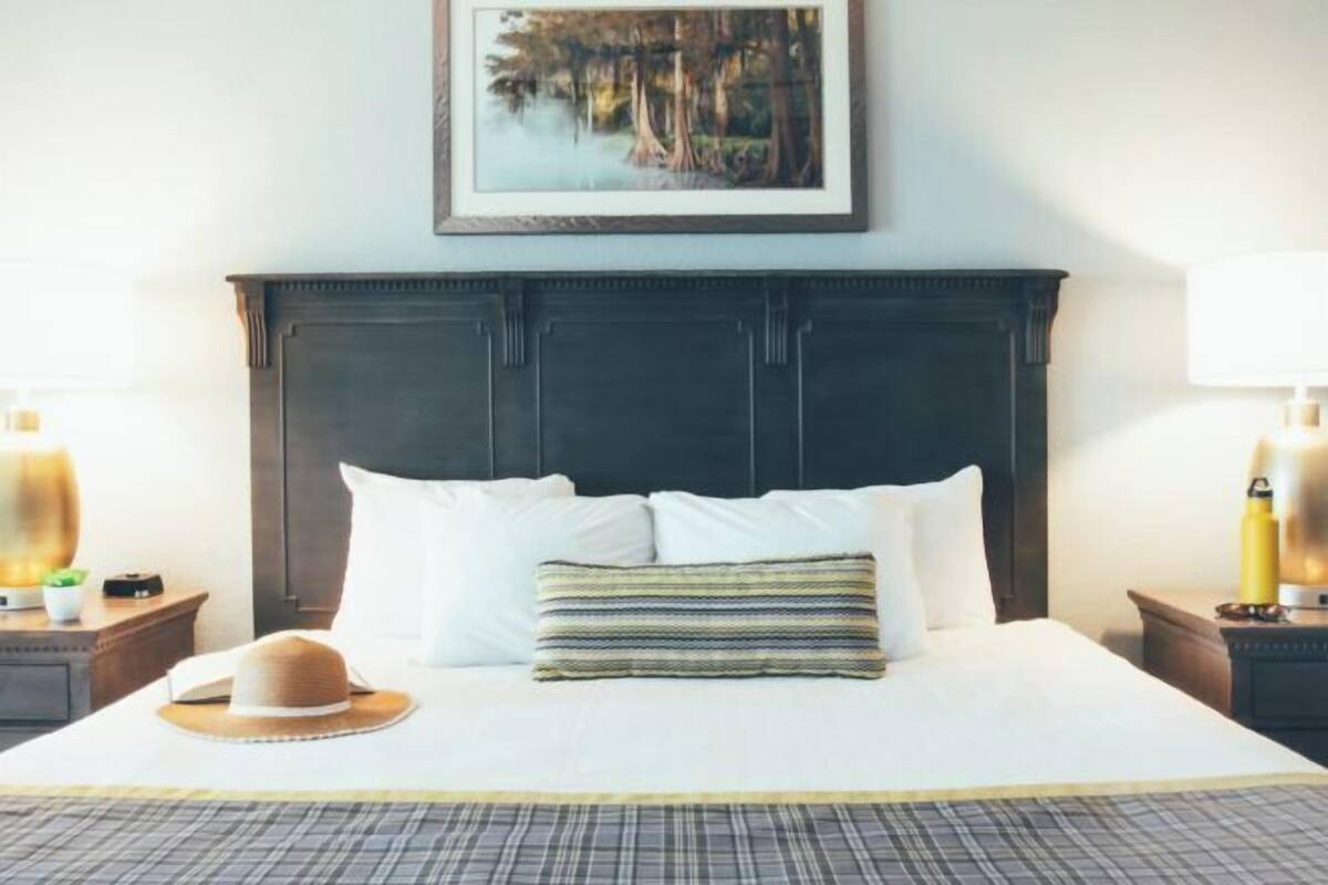 A hotel room with a large bed, a dark headboard, a framed picture on the wall, and a hat on the bed.