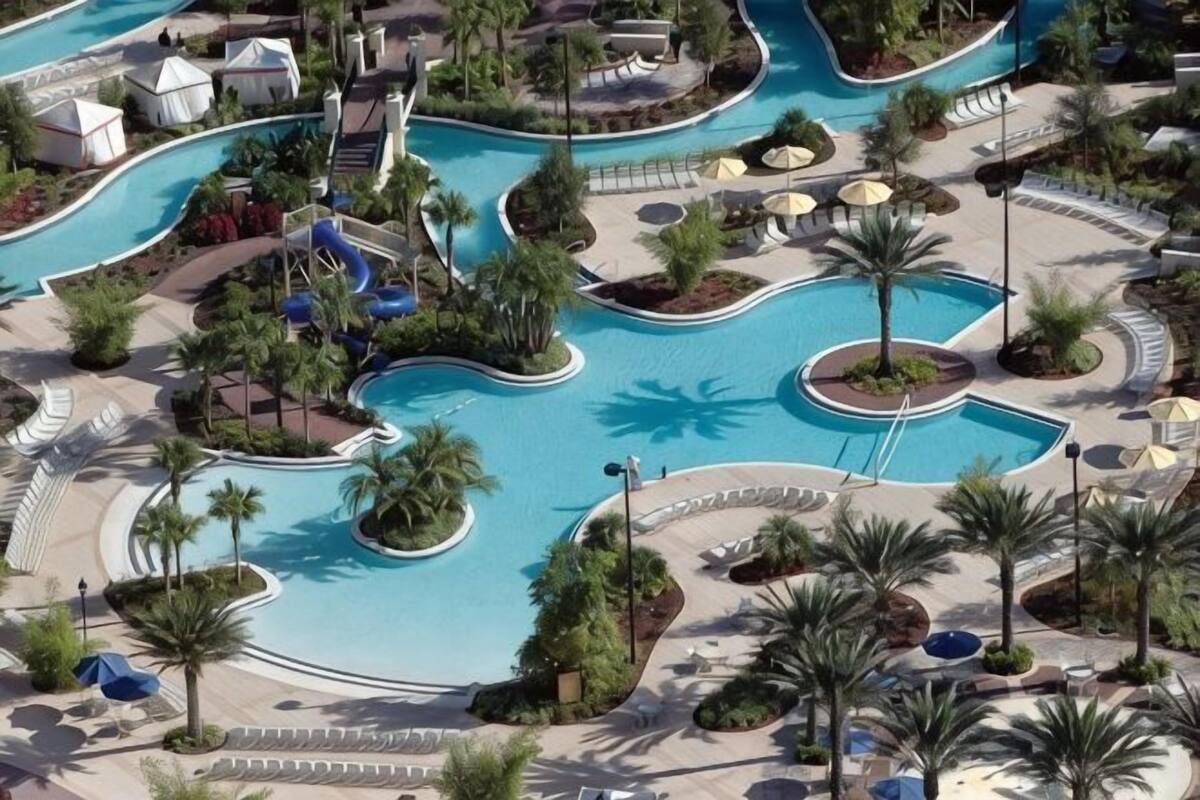 A large pool with multiple water slides, surrounded by palm trees and shaded areas.