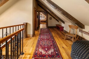 Eine Holztreppe mit Handlauf führt zu einem Schlafzimmer mit einem Bett und einer roten Bank.