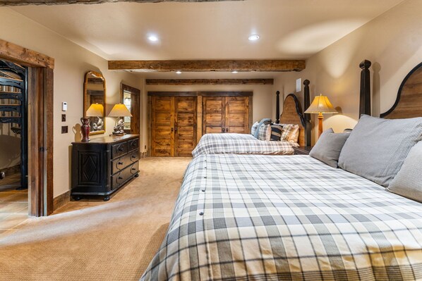 A bedroom with a large bed, a dresser, two lamps, and wooden doors. - The Restoration (Crested Butte)