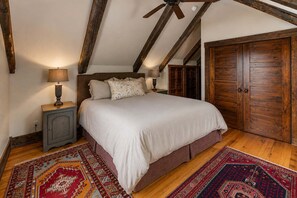 Ein Schlafzimmer mit einem großen Bett, Holzbalken, einem Kleiderschrank und zwei Nachttischen mit Lampen.