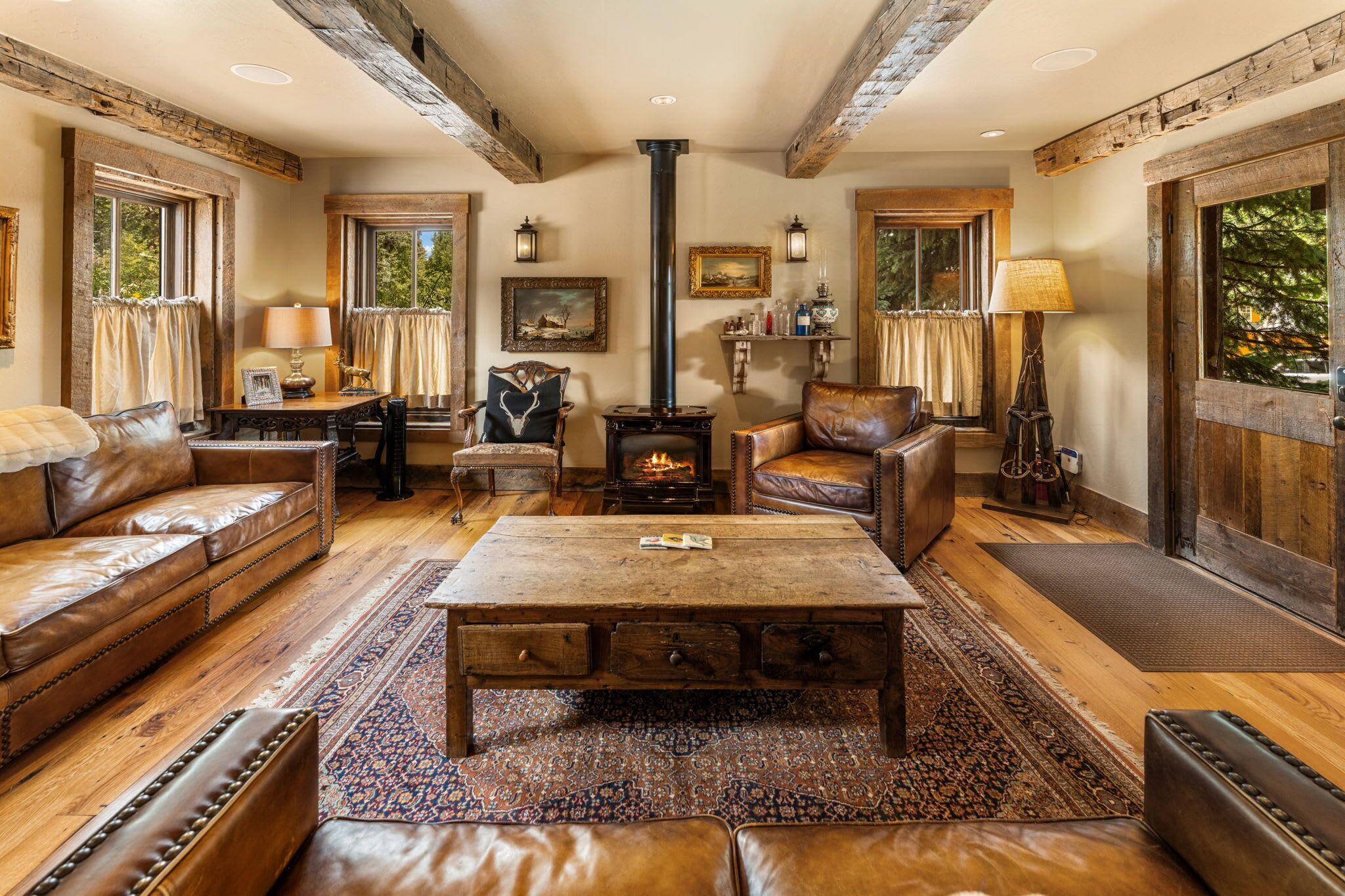 Un salon chaleureux avec des meubles en cuir, une table basse en bois placée au centre de la pièce, une cheminée et de grandes fenêtres.
