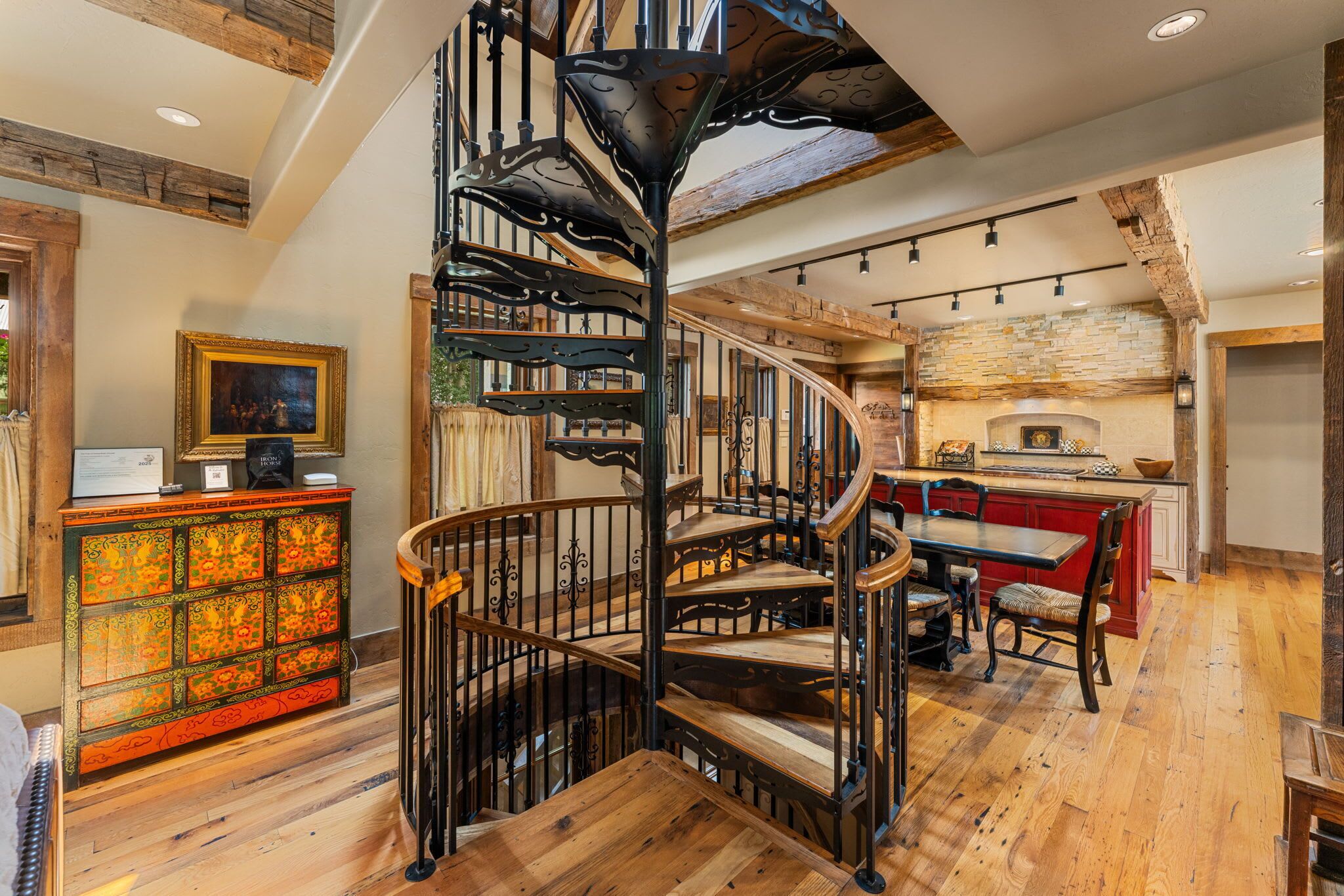 Eine Wendeltreppe mit Holzvertäfelung und Metallgeländern, die zu einem Essbereich mit rotem Tisch und Stühlen führt.