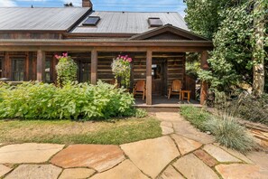 A log cabin with a stone pathway leading to the entrance, surrounded by lush greenery and a variety of plants. - The Restoration (Crested Butte)