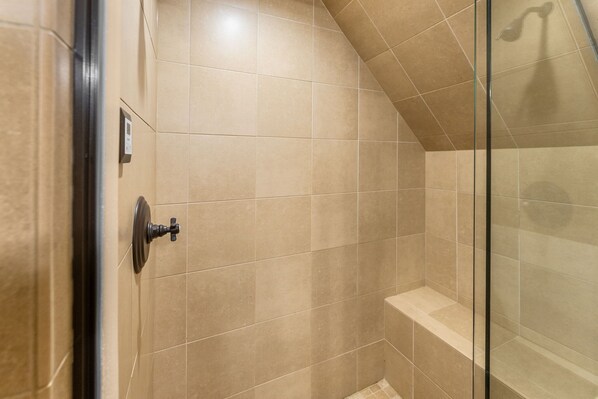 Une douche avec des carreaux de couleur beige et une porte en verre.