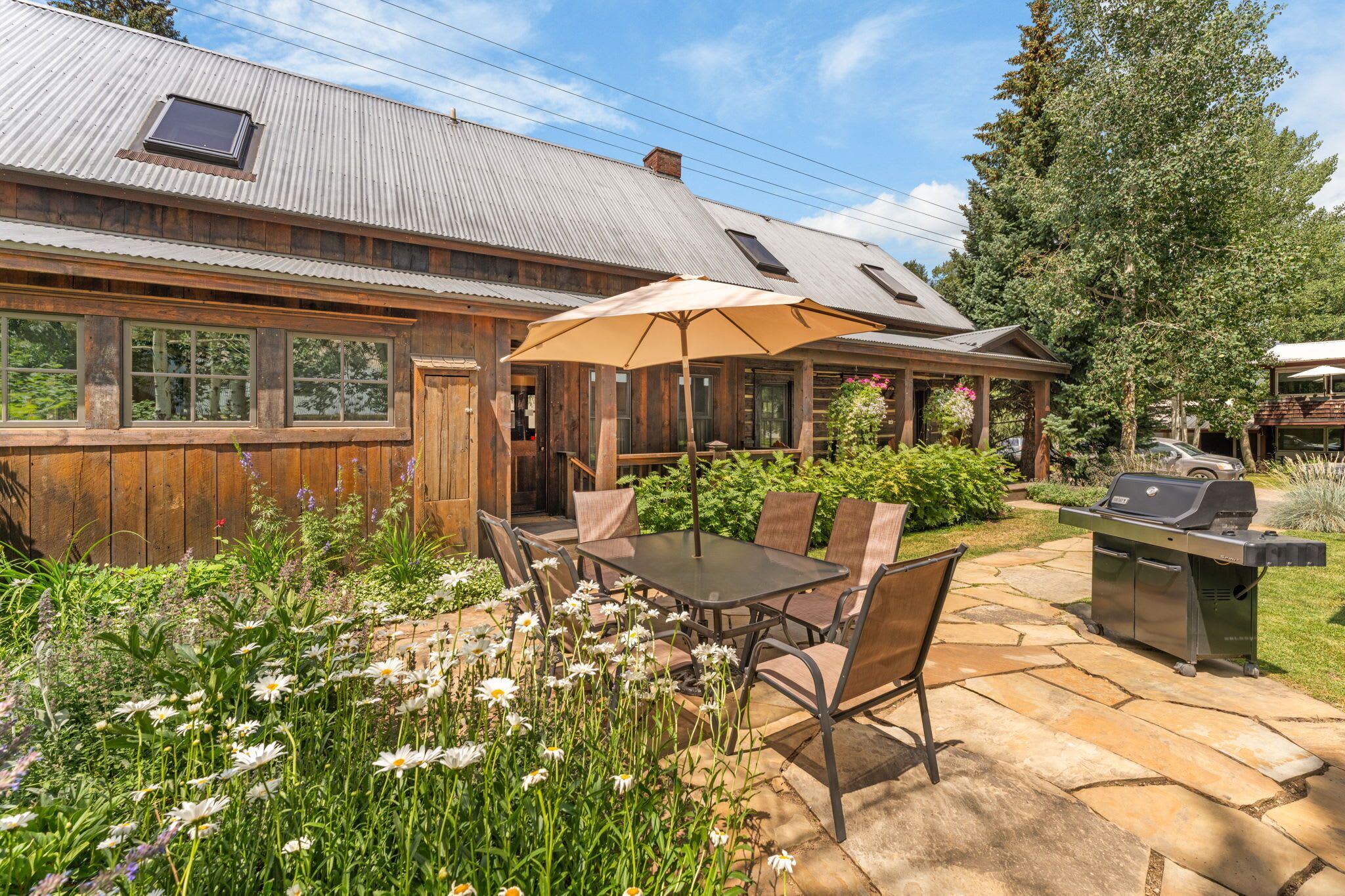Ein Holzhaus mit Terrasse, Sitzgelegenheit im Freien und einem Grill.