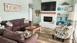 A living room with a brown sofa, a patterned armchair, a coffee table, and a fireplace with a TV above it. - Beautiful view of the beach, 3 bedroom-3 full bath, WiFi, cable, big deck (Galveston)