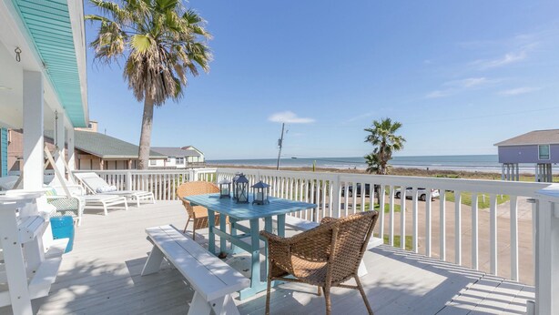 A wooden deck with a table and chairs, overlooking a beach. - Beautiful view of the beach, 3 bedroom-3 full bath, WiFi, cable, big deck (Galveston)
