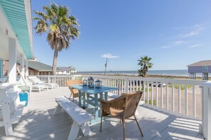 A wooden deck with a table and chairs, overlooking a beach.