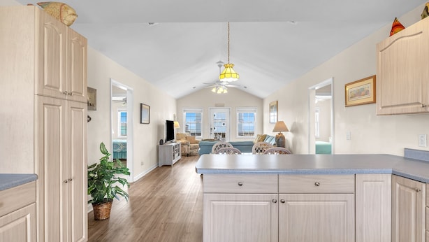 A spacious kitchen with light wood cabinetry, a central island, and a ceiling fan.