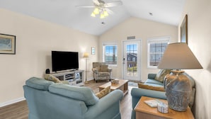 A living room with a flat-screen TV, a patterned armchair, a sofa, a coffee table, and a lamp.