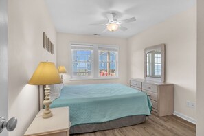 Un dormitorio con cama, cómoda, espejo, ventana y ventilador de techo.